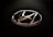 A chrome Hyundai logo with a sleek, rounded design is set against a textured black background, typically found on a steering wheel or vehicle interior.