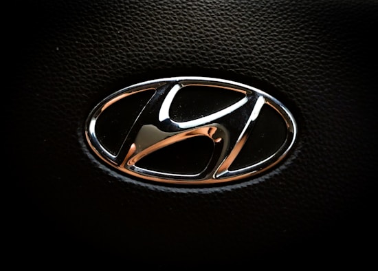 A chrome Hyundai logo with a sleek, rounded design is set against a textured black background, typically found on a steering wheel or vehicle interior.