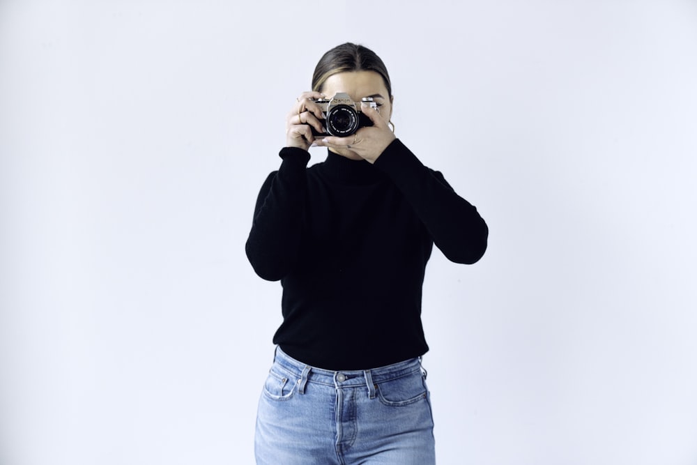 woman in black long sleeve shirt and blue denim jeans holding black and silver camera
