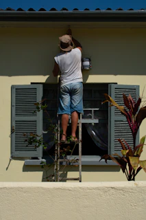 woman in white shirt and blue denim shorts standing on white and gray ladder during daytime