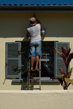 woman in white shirt and blue denim shorts standing on white and gray ladder during daytime