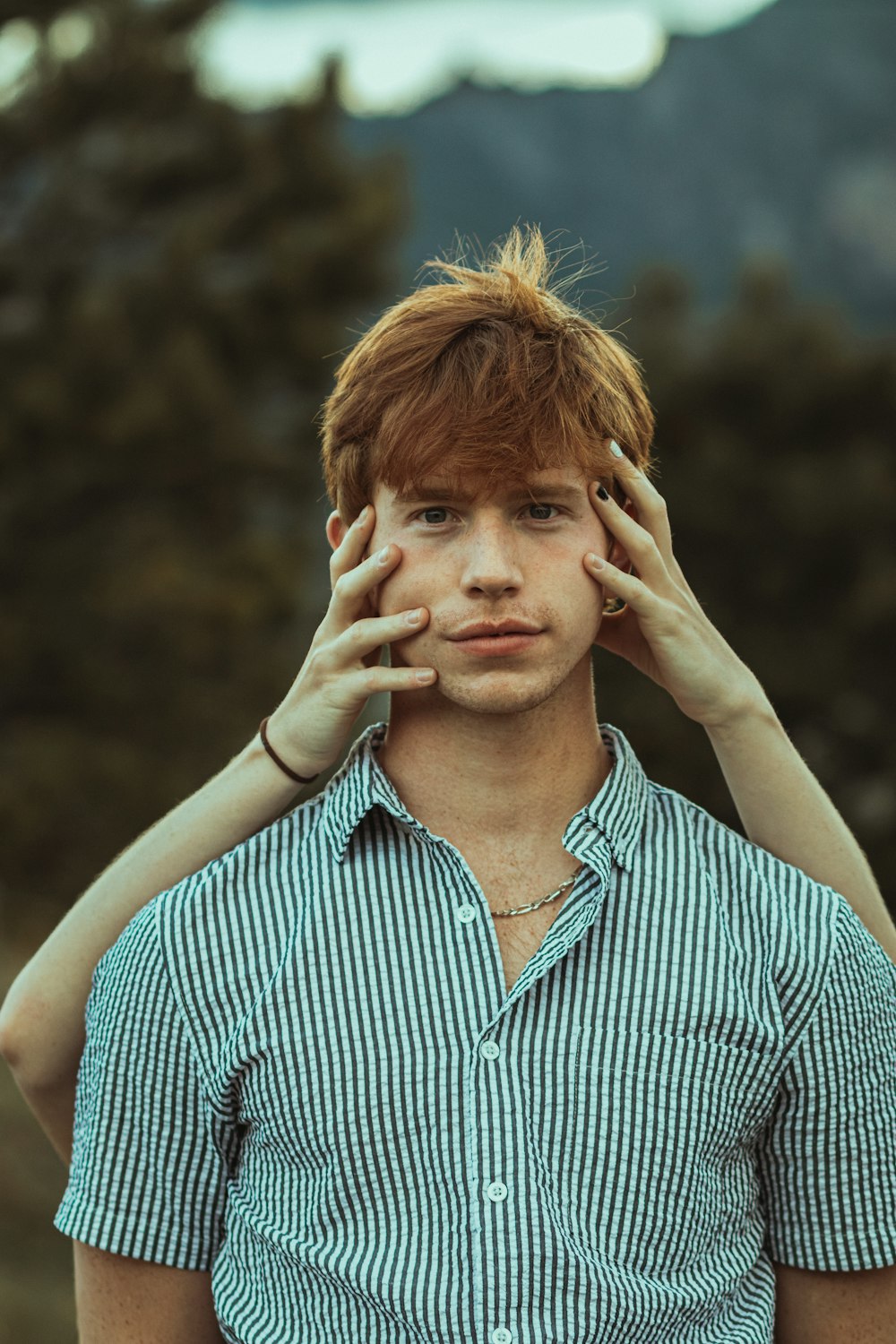 man in blue and white striped button up shirt covering his face