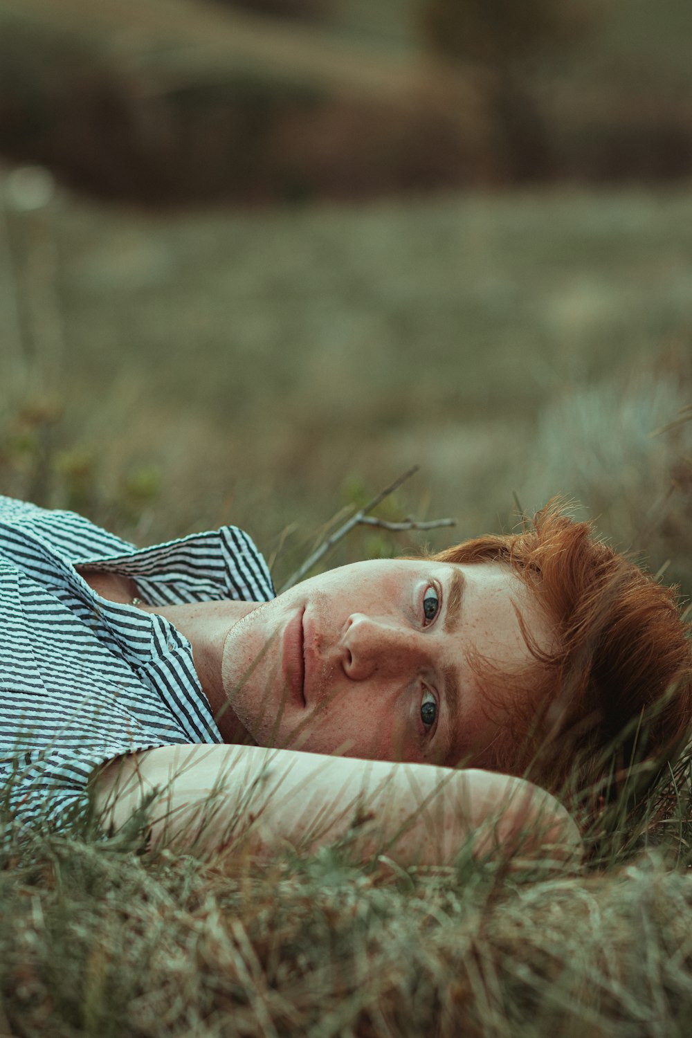 woman in white and black striped shirt lying on green grass during daytime