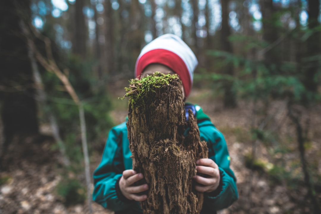 child in blue jacket and white knit cap holding brown tree trunk