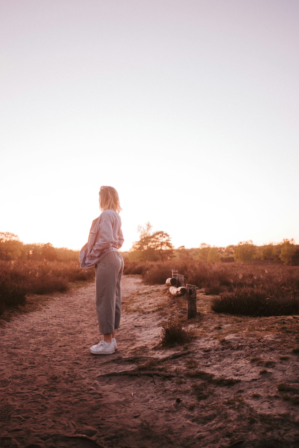 woman in brown long sleeve shirt and gray pants standing on brown grass field during daytime