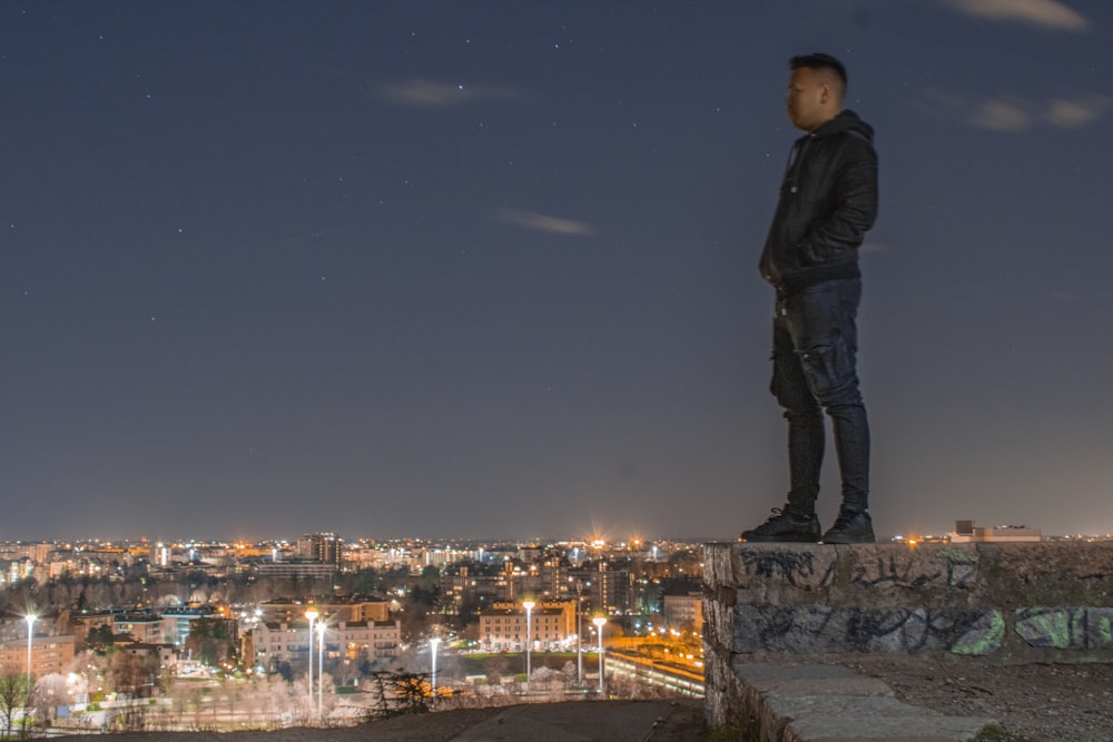 man in black jacket standing on rock during night time