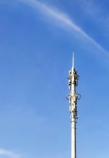 A tall communication tower with various antennas and dishes, set against a clear blue sky. The tower has multiple platforms and technical equipment attached at intervals along its height.