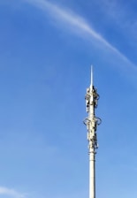 A tall communication tower with various antennas and dishes, set against a clear blue sky. The tower has multiple platforms and technical equipment attached at intervals along its height.