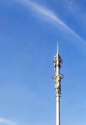 A tall communication tower with various antennas and dishes, set against a clear blue sky. The tower has multiple platforms and technical equipment attached at intervals along its height.