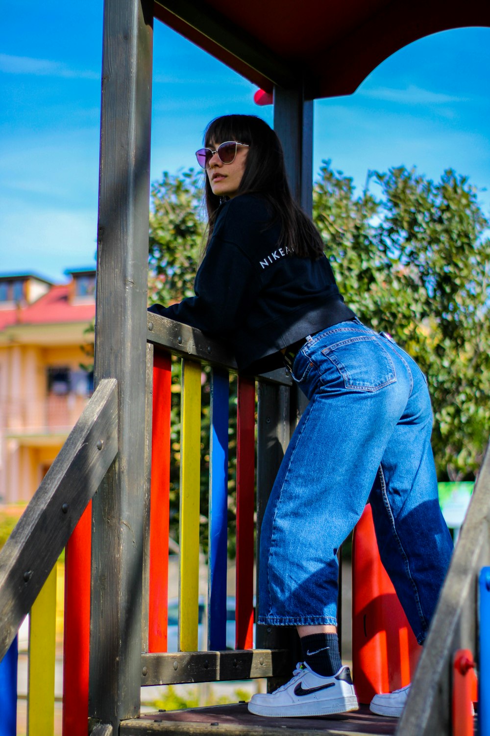 woman in black hoodie and blue denim jeans standing beside brown wooden railings during daytime
