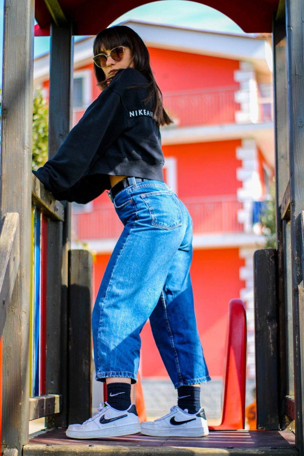 woman in black hoodie and blue denim jeans standing beside brown wooden post during daytime