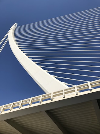 A modern suspension bridge with white cables and a sleek new-age design against a clear blue sky. The architectural lines create a harmonious pattern, emphasizing elegance and innovation.