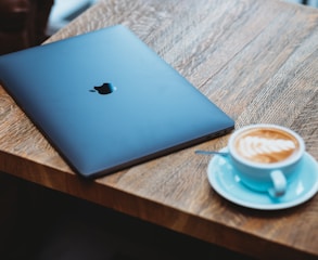 silver macbook beside white ceramic mug on brown wooden table