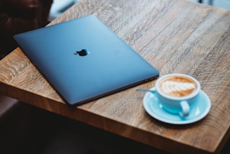 silver macbook beside white ceramic mug on brown wooden table