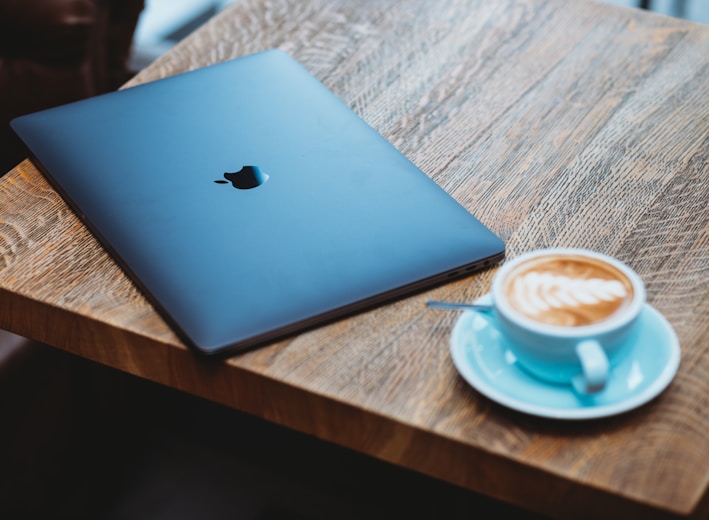 silver macbook beside white ceramic mug on brown wooden table