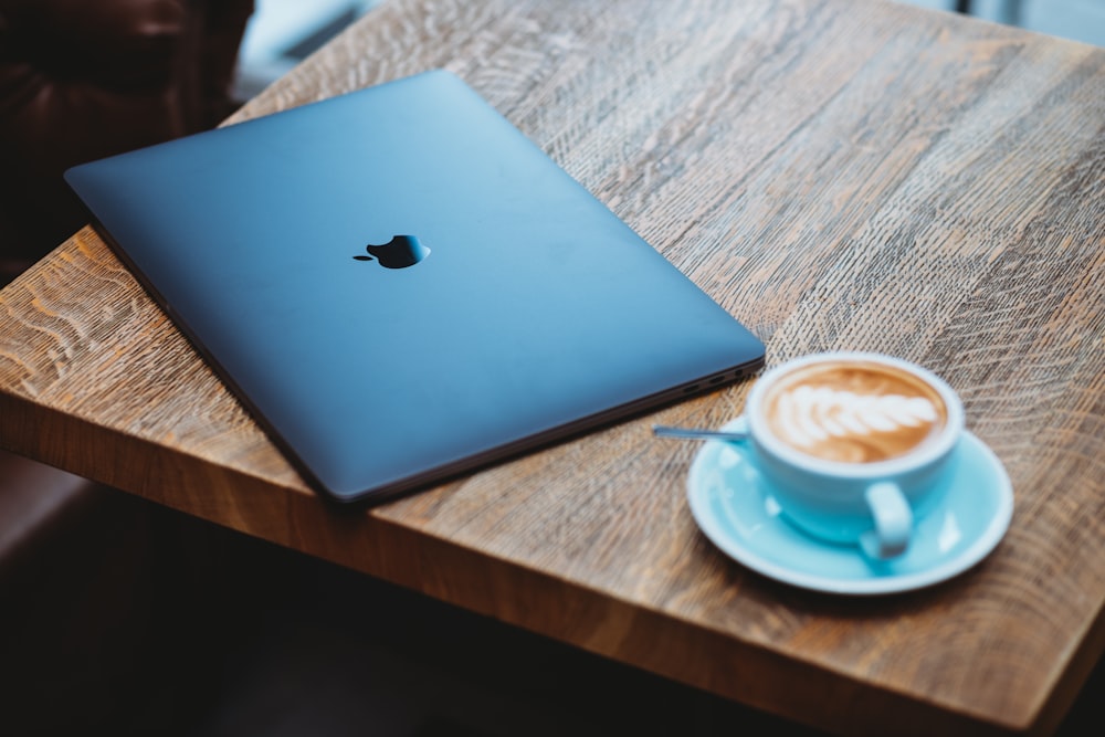 MacBook argenté à côté d’une tasse en céramique blanche sur une table en bois marron