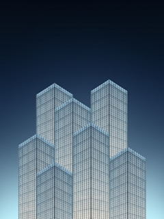 A cluster of modern skyscrapers with a sleek, glass facade is set against a deep blue gradient sky. The geometric design creates an optical illusion of the towers interlocking like puzzle pieces.