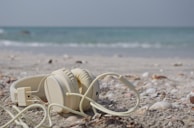 Wireless earbuds resting beside a sunhat and sunglasses on a sandy beach.
