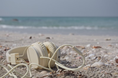 Bluetooth wireless earbuds beside a smartphone on a sandy beach towel.