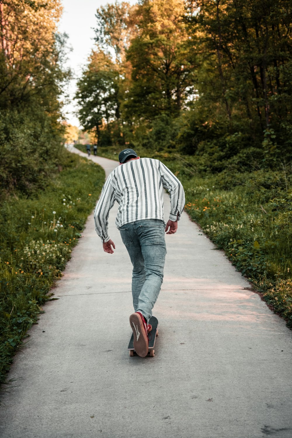 donna in camicia a maniche lunghe a righe bianche e nere e jeans in denim blu che camminano sul sentiero