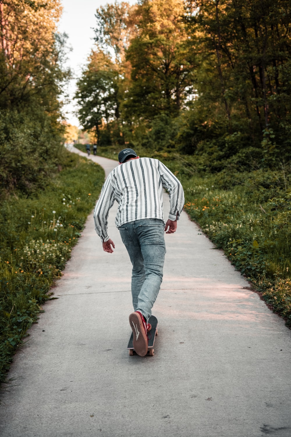 woman in white and black striped long sleeve shirt and blue denim jeans walking on pathway