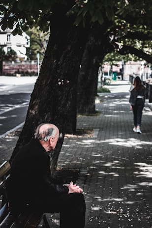 An elderly man sitting on a park bench, gazing thoughtfully into the distance.