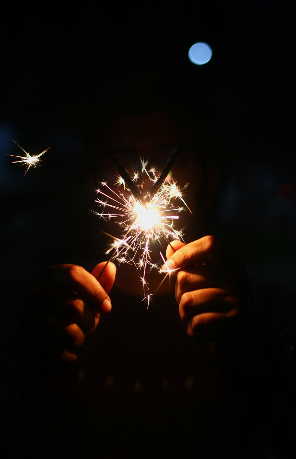person holding lighted sparkler in dark room
