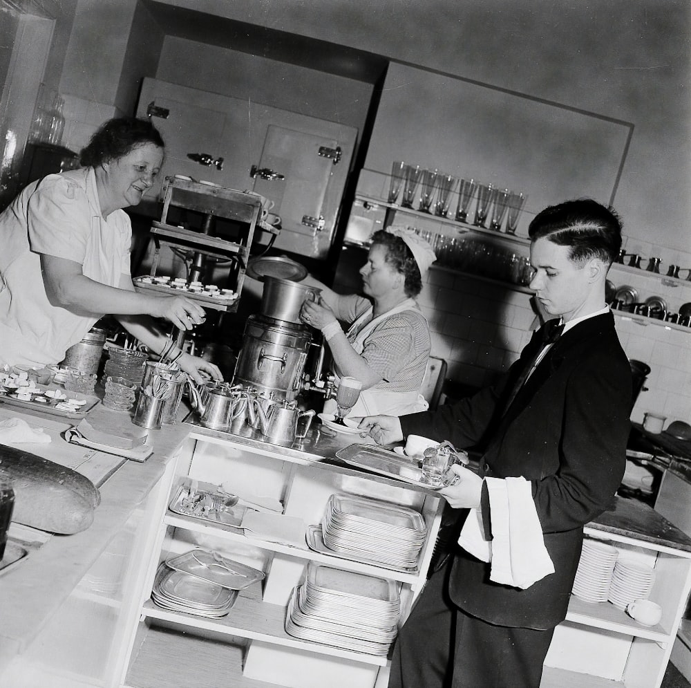 grayscale photo of man and woman standing in front of kitchen sink