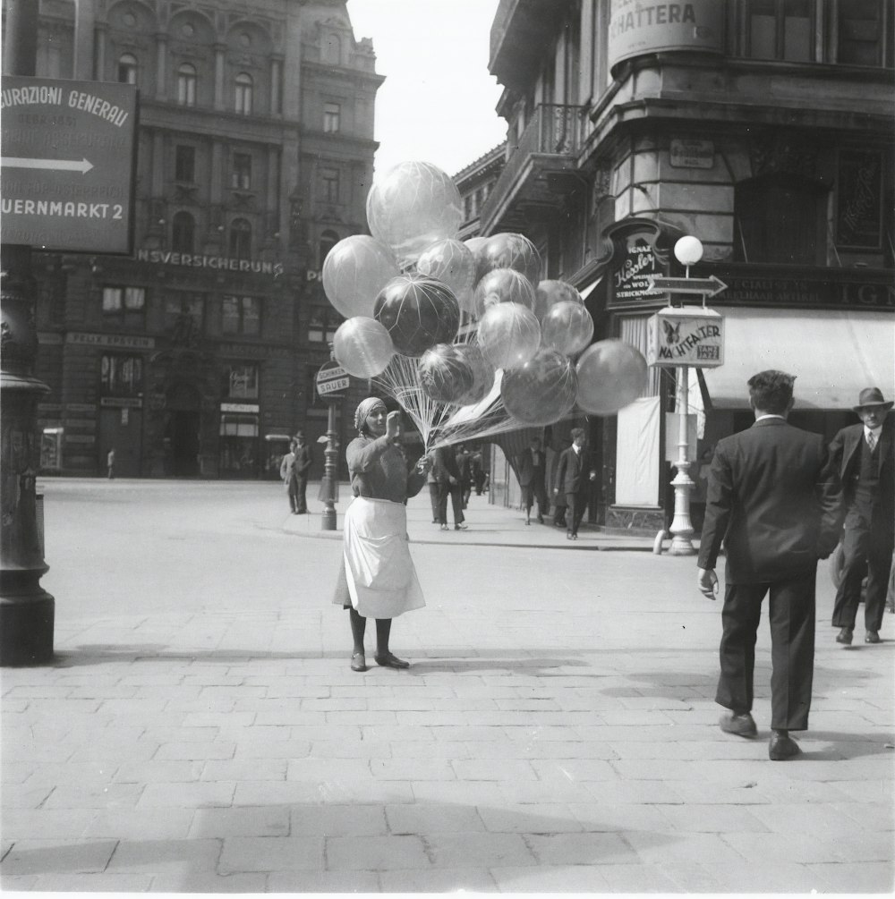 foto em escala de cinza de pessoas andando na calçada com balões