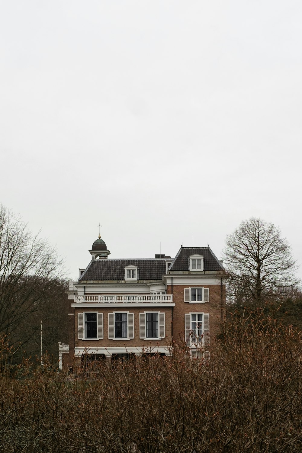 brown and white concrete house near bare trees under white sky during daytime