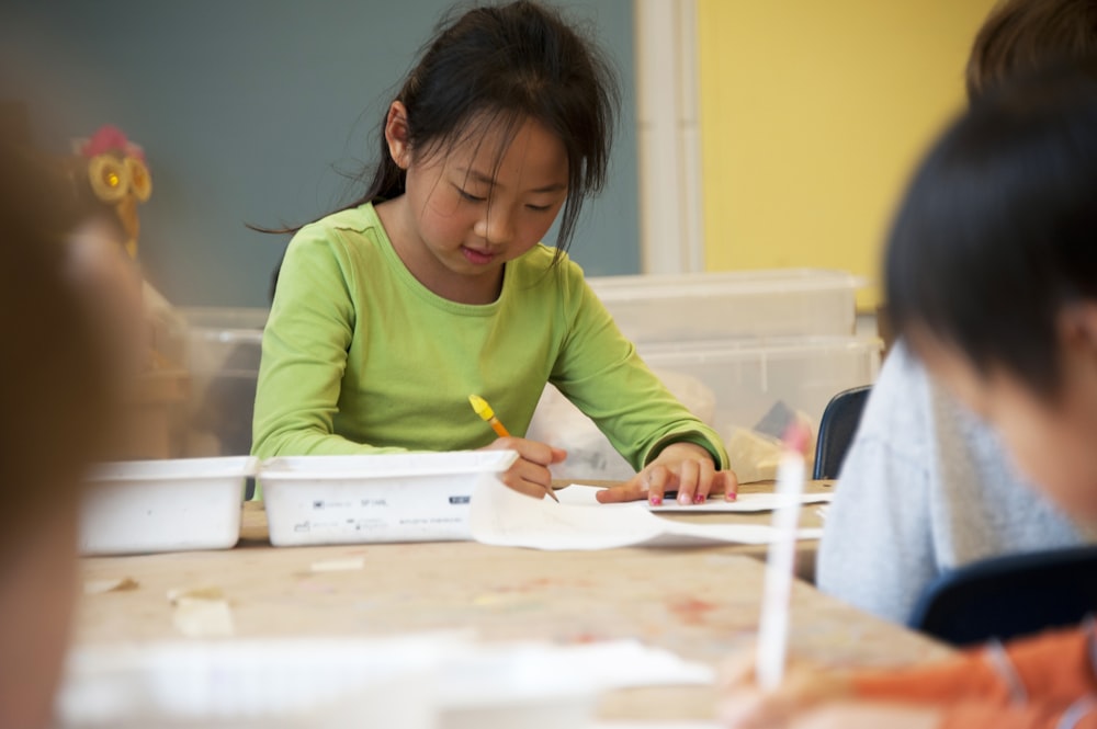 girl in green crew neck t-shirt writing on white paper