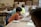 Children are seated around a table in a classroom setting, engaging in activities with paper and art supplies. The classroom appears busy with students focused and collaborating on creative tasks.