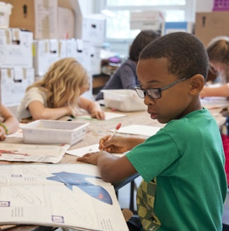 boy in green sweater writing on white paper