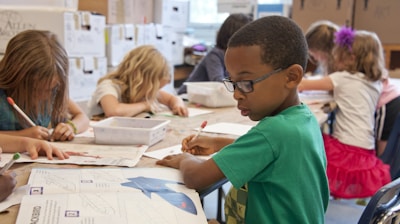 boy in green sweater writing on white paper