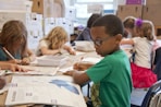 boy in green sweater writing on white paper