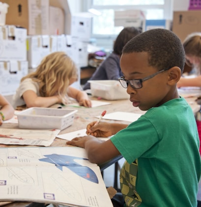 boy in green sweater writing on white paper