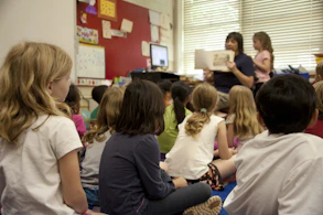 A cozy classroom scene where kids and a storyteller gather around a glowing book.