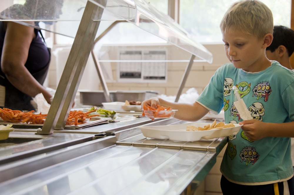 Junge im grünen Rundhals-T-Shirt steht vor Essen auf dem Tisch