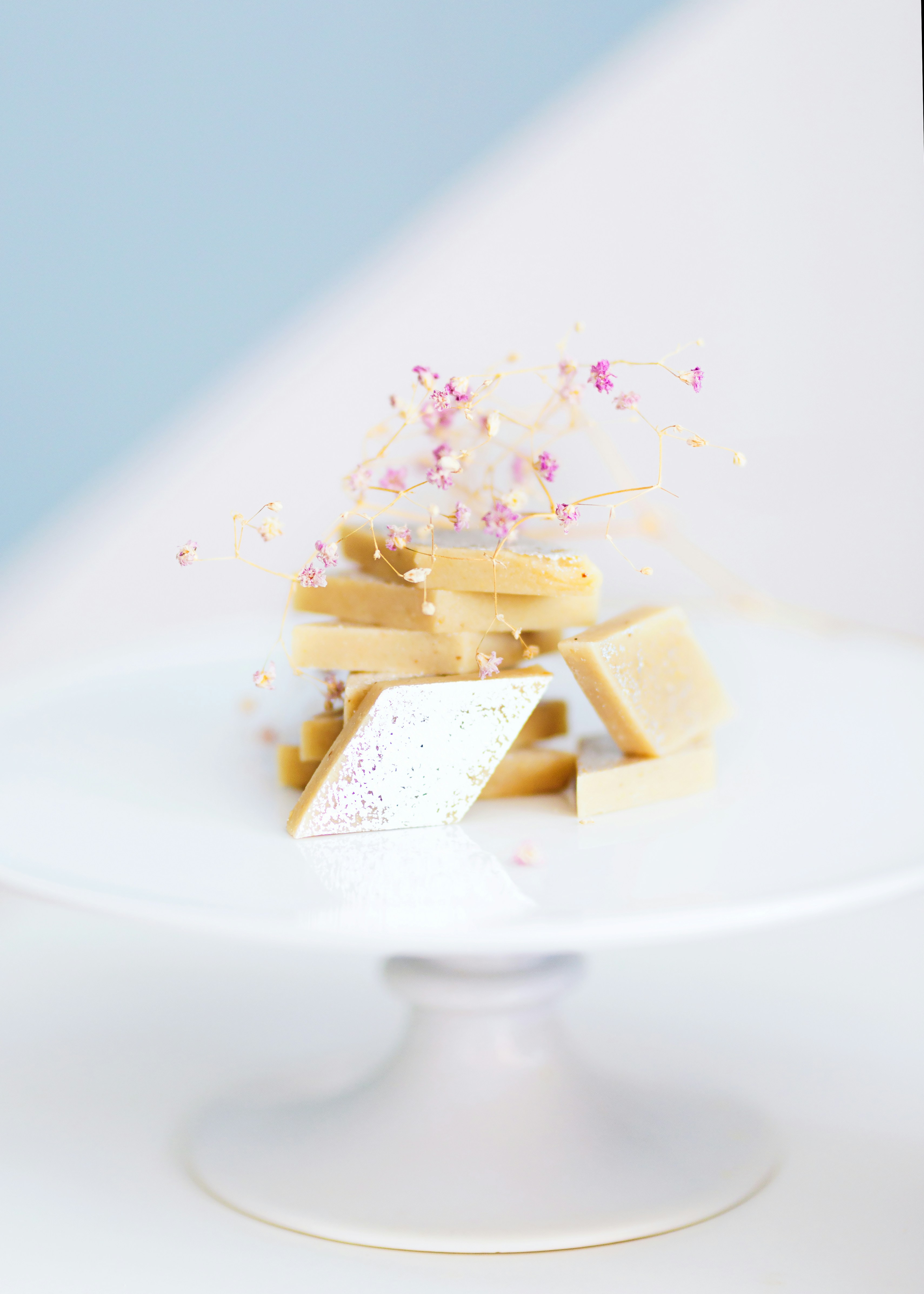 Diamond-cut white and golden Barfi Indian sweet on silver tray with rose petals