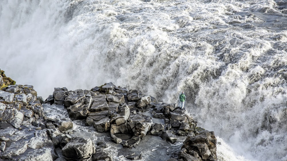 person in green jacket standing on rocky shore during daytime