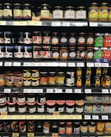 Assorted gourmet jam jars arranged on a wooden shelf with natural lighting.