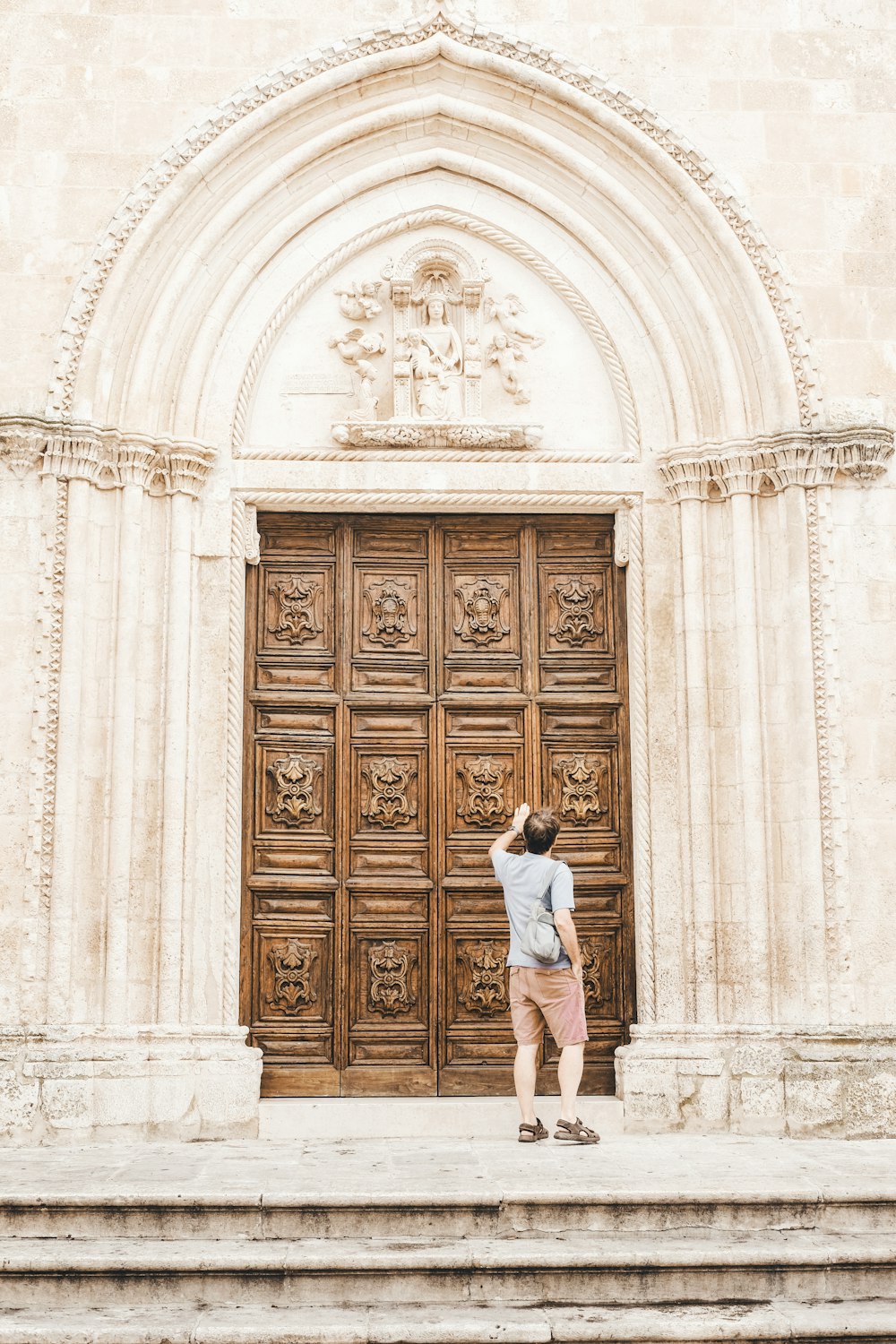 Mujer con camisa blanca de pie frente a una puerta de madera marrón