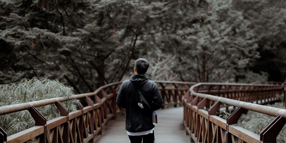 man in black jacket and white pants walking on bridge