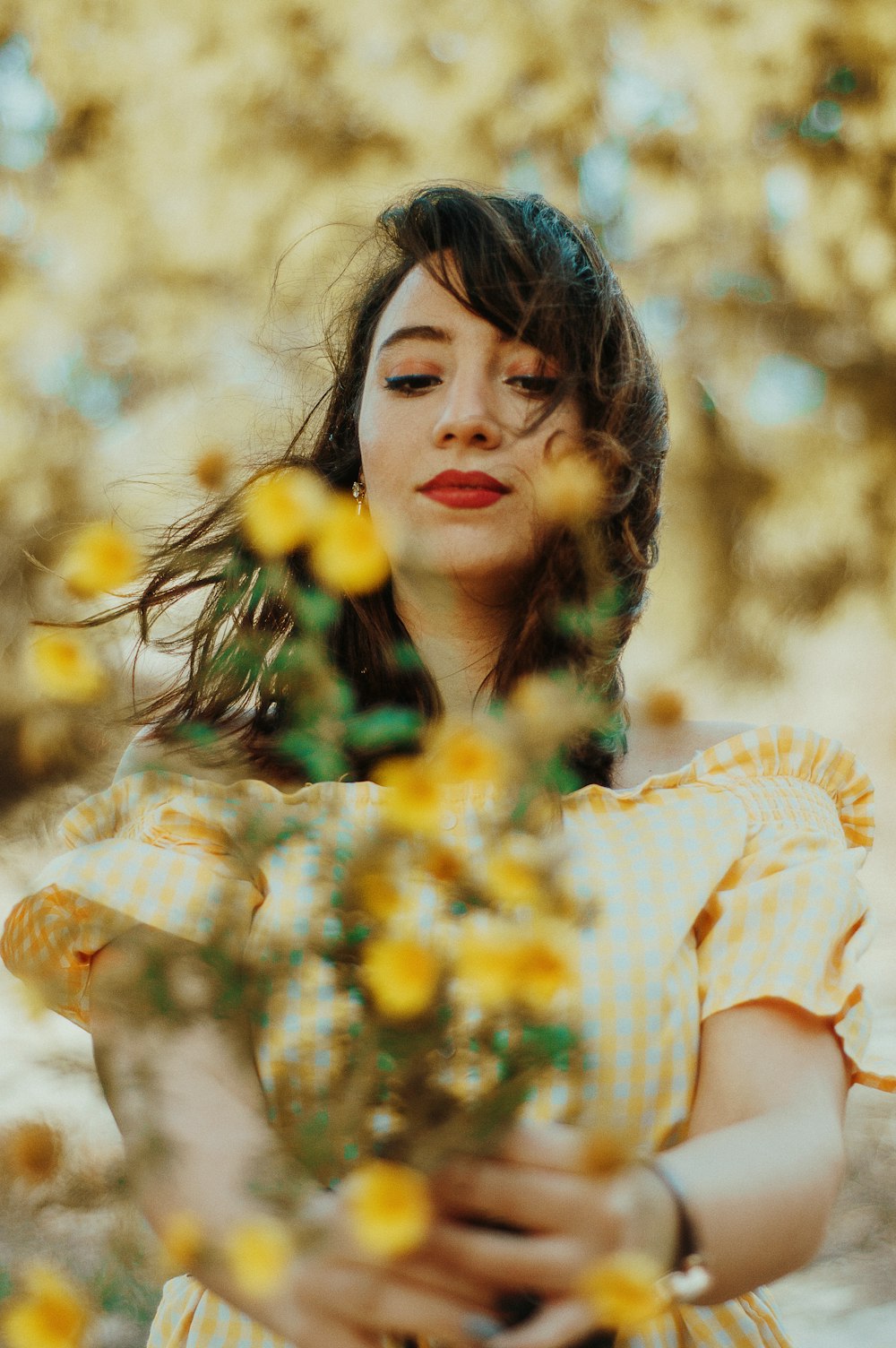 woman in white and brown stripe shirt holding yellow flowers