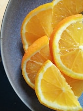 Slices of fresh oranges are neatly arranged on a dark plate, highlighting the bright, juicy interior and vibrant orange peel.