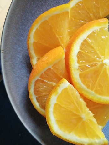 Slices of fresh oranges are neatly arranged on a dark plate, highlighting the bright, juicy interior and vibrant orange peel.