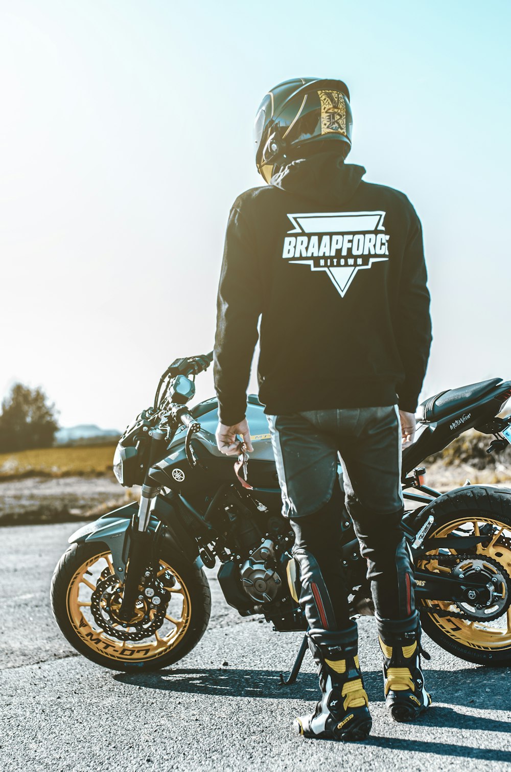 man in black hoodie and blue denim jeans standing beside black motorcycle during daytime