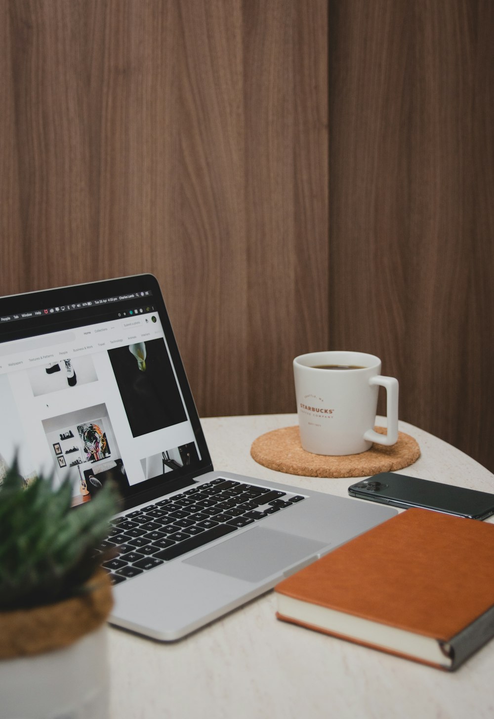 macbook pro beside white ceramic mug on brown wooden table