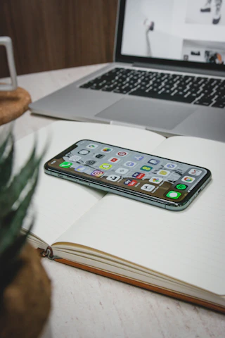 A cozy workspace with a smartphone displaying the Habit Haven app interface surrounded by plants and a notebook.