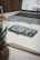 A smartphone displaying various app icons rests on an open notebook with lined pages. In the background, there is a laptop with a partially visible screen showing images. A plant in the foreground adds a touch of greenery to the scene.